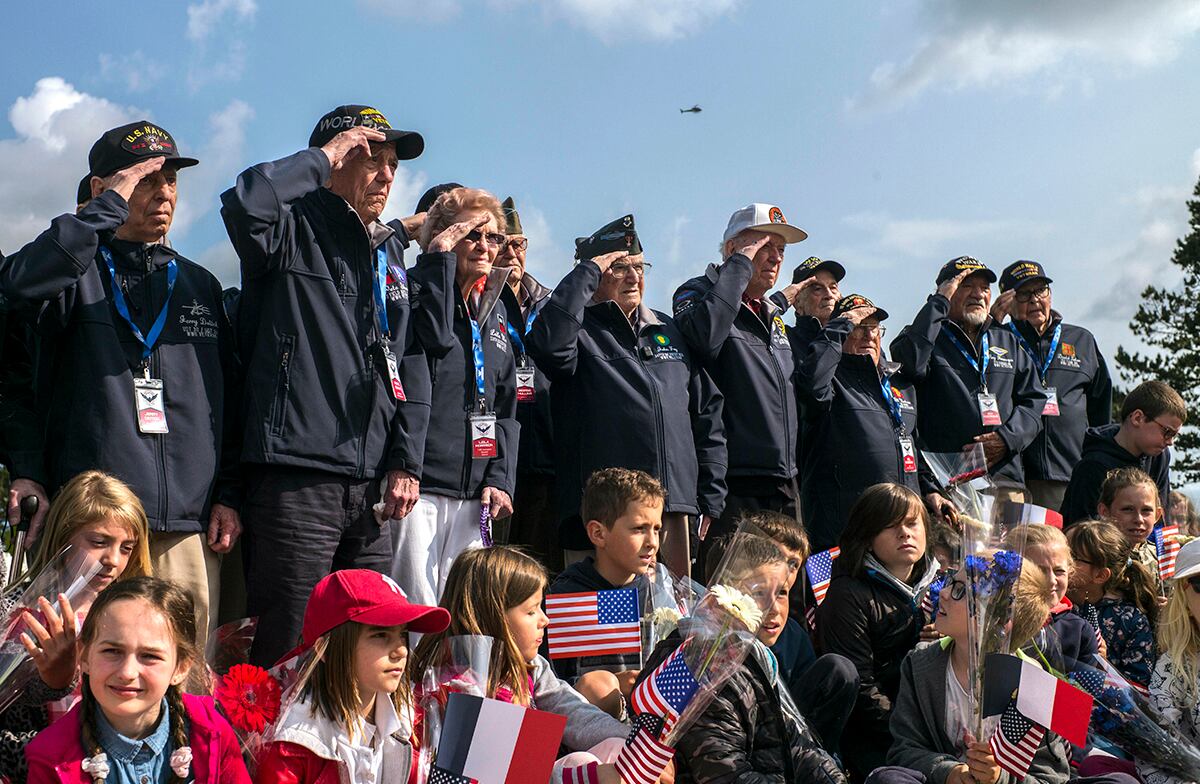 World War II veterans from the United States salute as they pose with local school children at the Normandy American Cemetery in Colleville-sur-Mer, Normandy, France