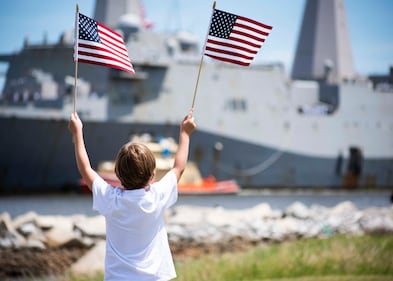 A family member waives American flags as the San Antonio-class amphibious transport dock ship USS New York (LPD 21) arrives at Naval Station Mayport in Florida on July 28, 2020.