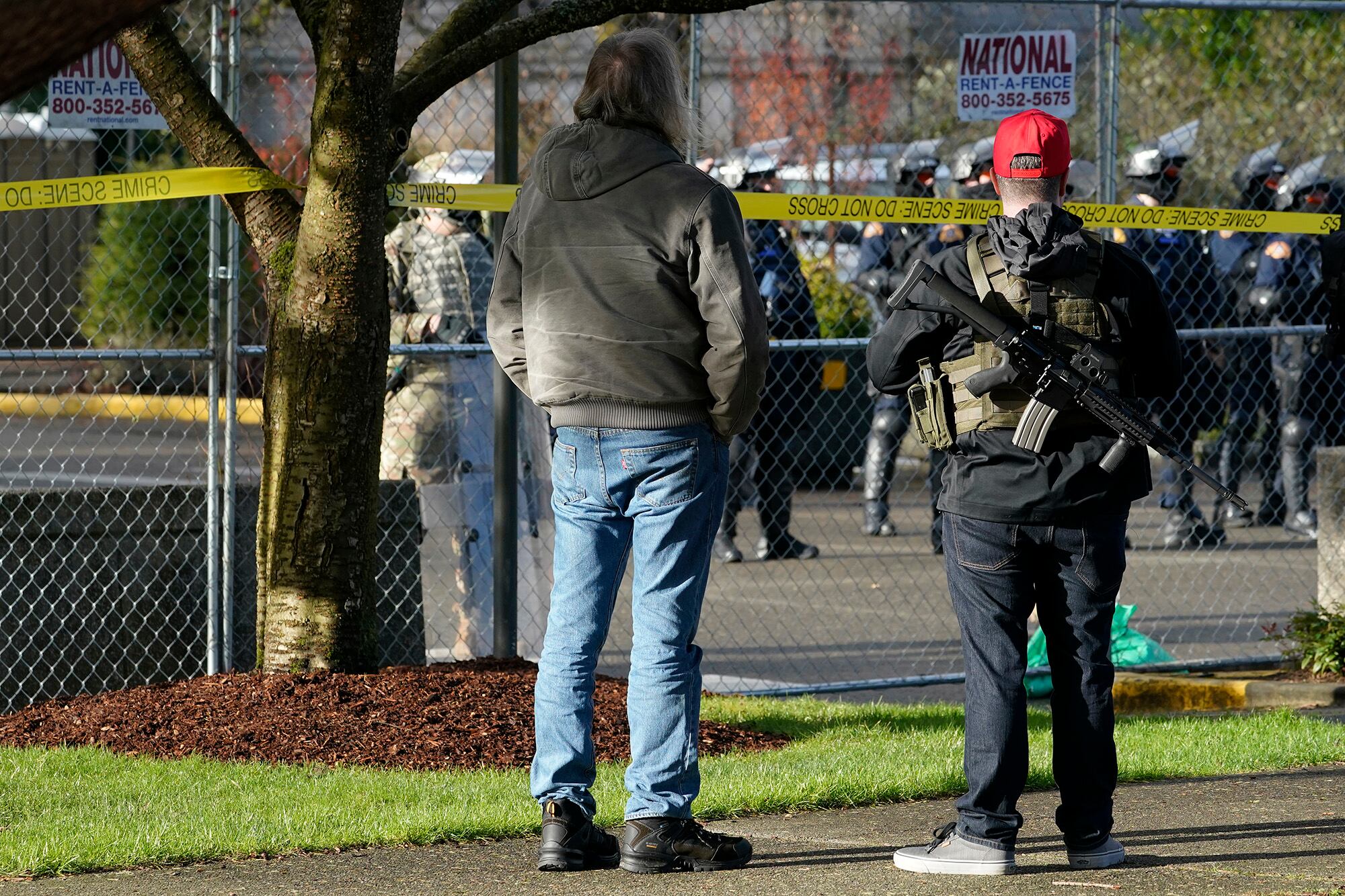 An armed supporter of President Donald Trump looks in at a gathering of Washington State Patrol troopers behind a perimeter fence during a rally, Sunday, Jan. 10, 2021, at the Capitol in Olympia, Wash.